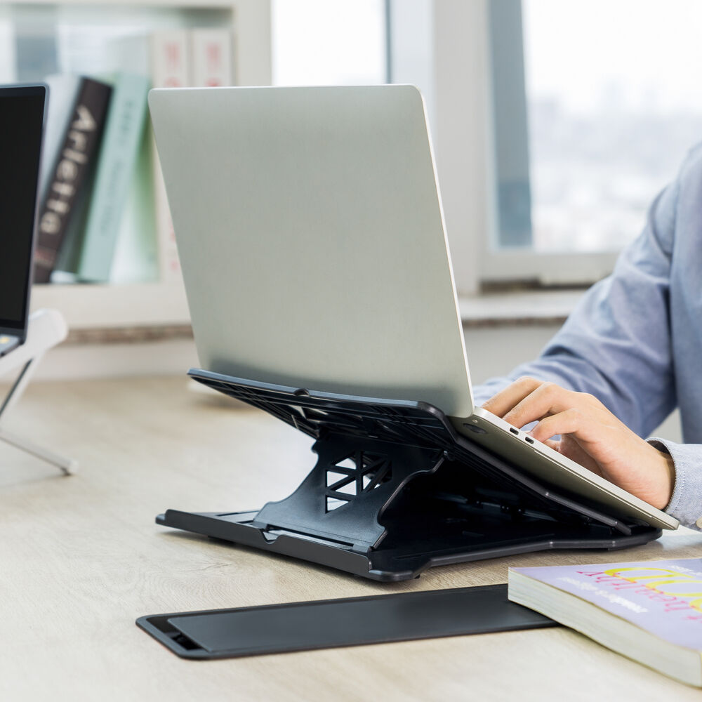 A laptop rests on a black stand on a wooden desk. Hands are typing on the keyboard.