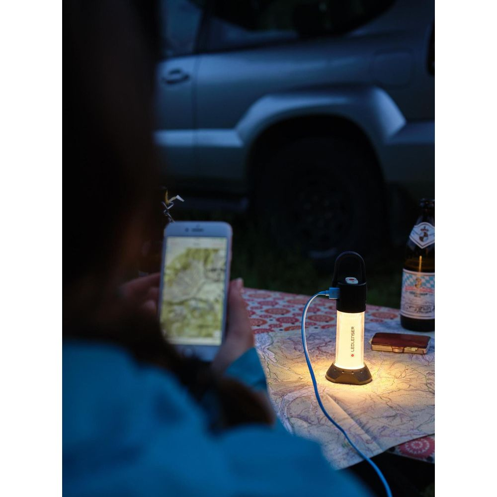 Eine Person hält ein Handy mit Karte. Eine Lampe leuchtet, daneben eine Flasche.