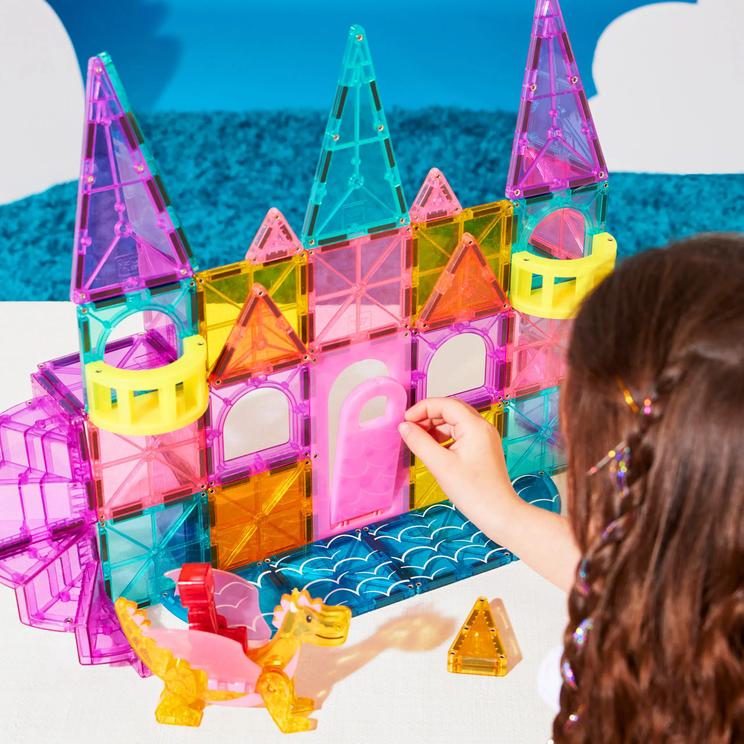 Ein Kind baut eine bunte Burg aus Magnetbausteinen mit einem Drachen.