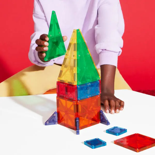 Un enfant construit une tour fusée colorée avec des blocs de construction magnétiques transparents.
