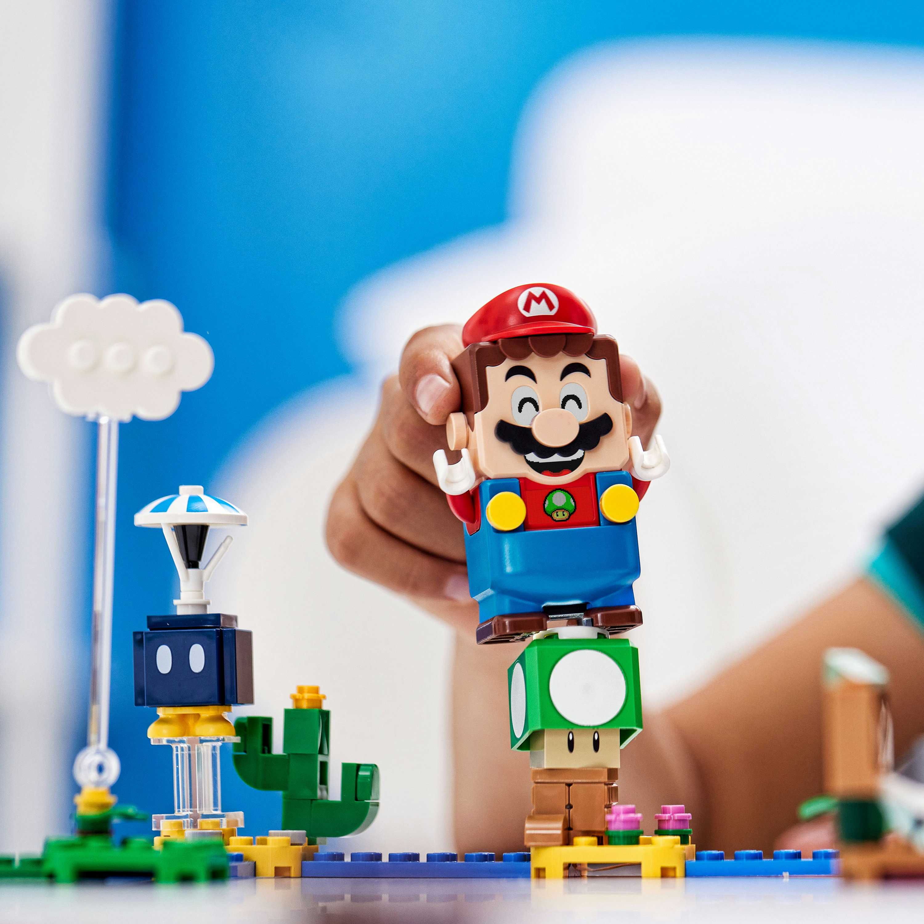 Figurine Mario sur un bloc champignon, avec un cactus et un nuage à proximité.