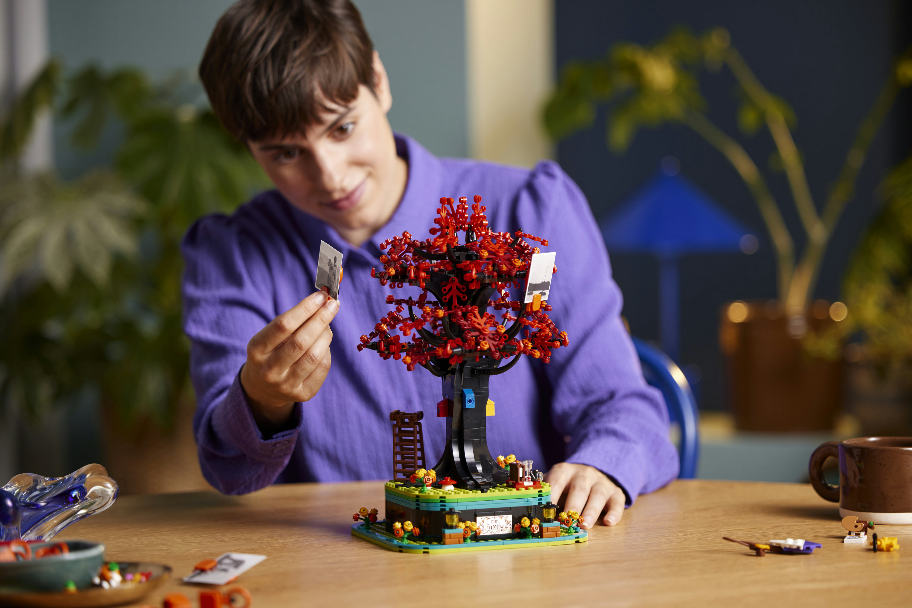 Een persoon in een paars shirt houdt een foto naast een LEGO-boom.