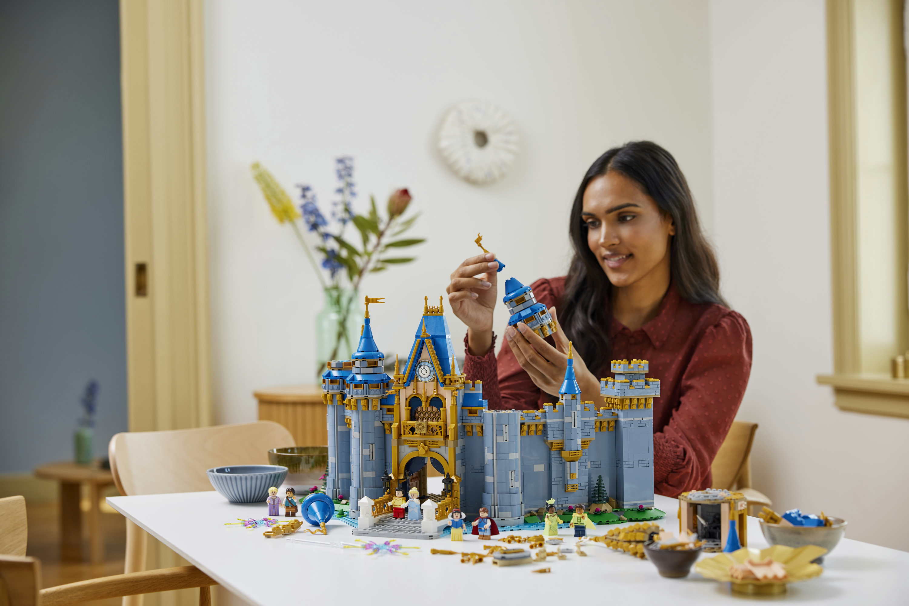 Una donna costruisce un castello Lego blu e oro con minifigure su un tavolo bianco.