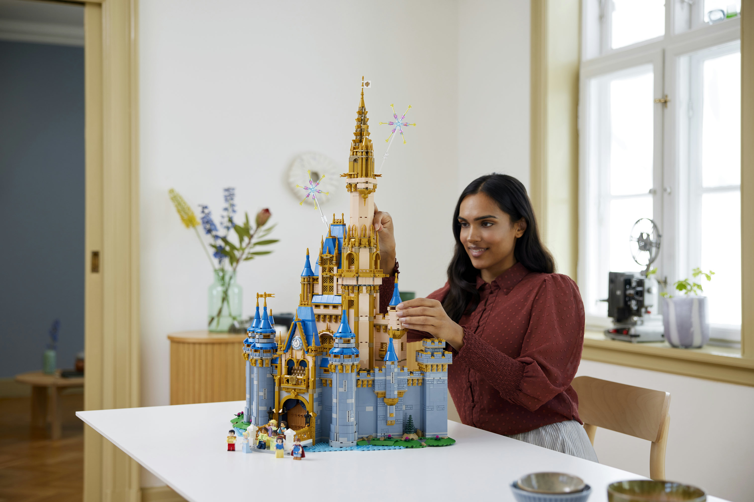 Una donna costruisce una dettagliata versione Lego del castello Disney in una stanza luminosa.