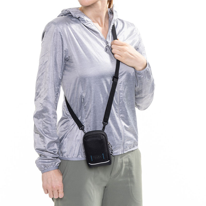 Een persoon draagt een grijze jas en een zwarte crossbody tas met TENBA logo.