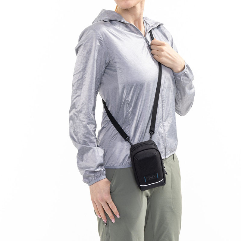 Een vrouw draagt een grijze jas en een zwarte crossbody tas.