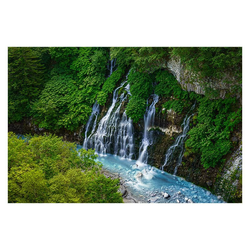 A lush waterfall cascades over mossy rocks into a vibrant blue river.