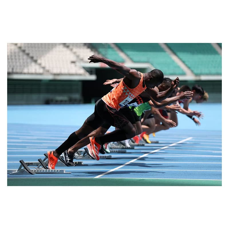 Athletes in starting blocks on a blue track, poised for a sprint.