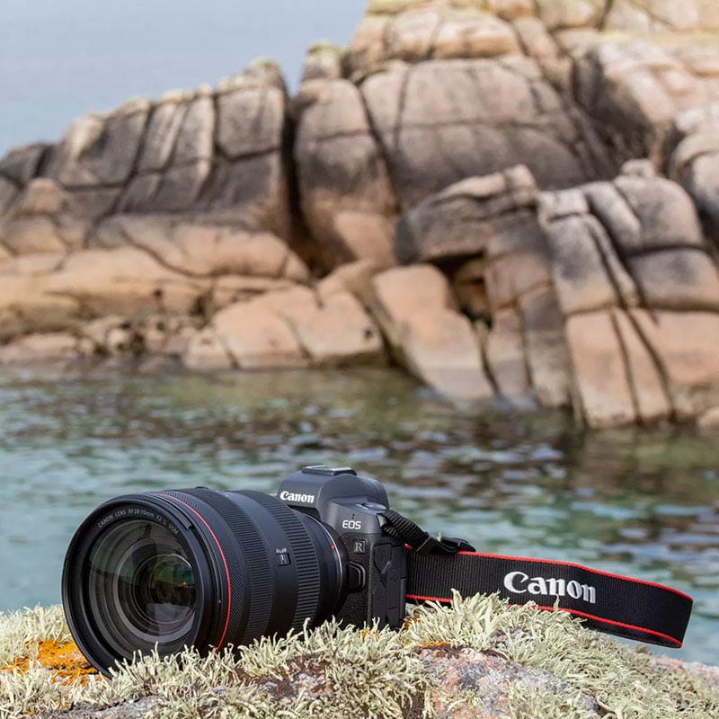 Una cámara Canon con objetivo descansa sobre una roca musgosa junto al agua.