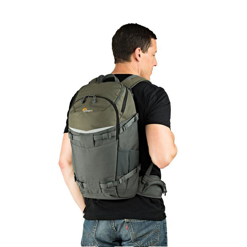 Hombre con camisa negra y jeans lleva una mochila gris y verde.