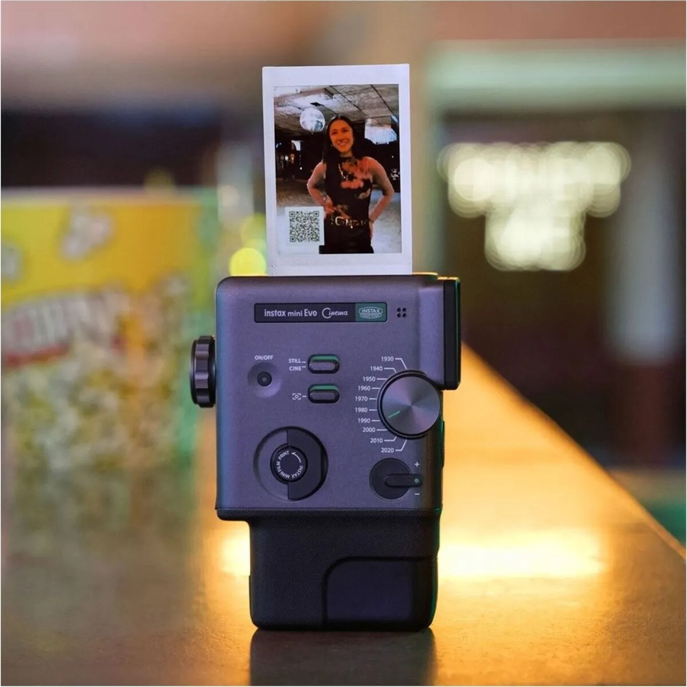 Instax Mini Evo kamera bir kadının fotoğrafını basıyor. Patlamış mısır arka planda bulanık.