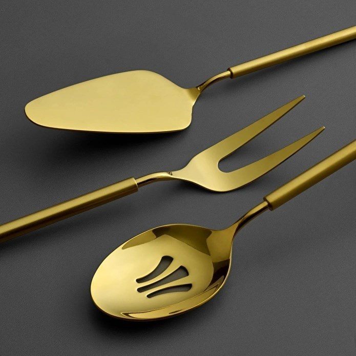 Altın rengi pasta spatulası, çatal ve süzgeçli kaşık koyu zeminde.