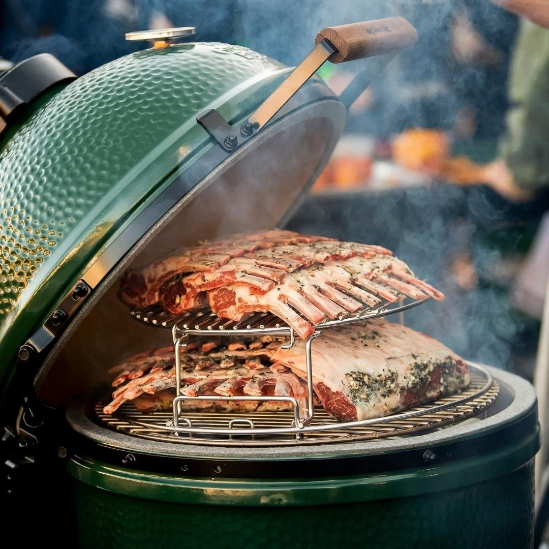 Otlarla tatlandırılmış iki çiğ kuzu pirzola, yeşil bir Big Green Egg ızgaranın içinde kademeli bir rafta ızgara yapılıyor.