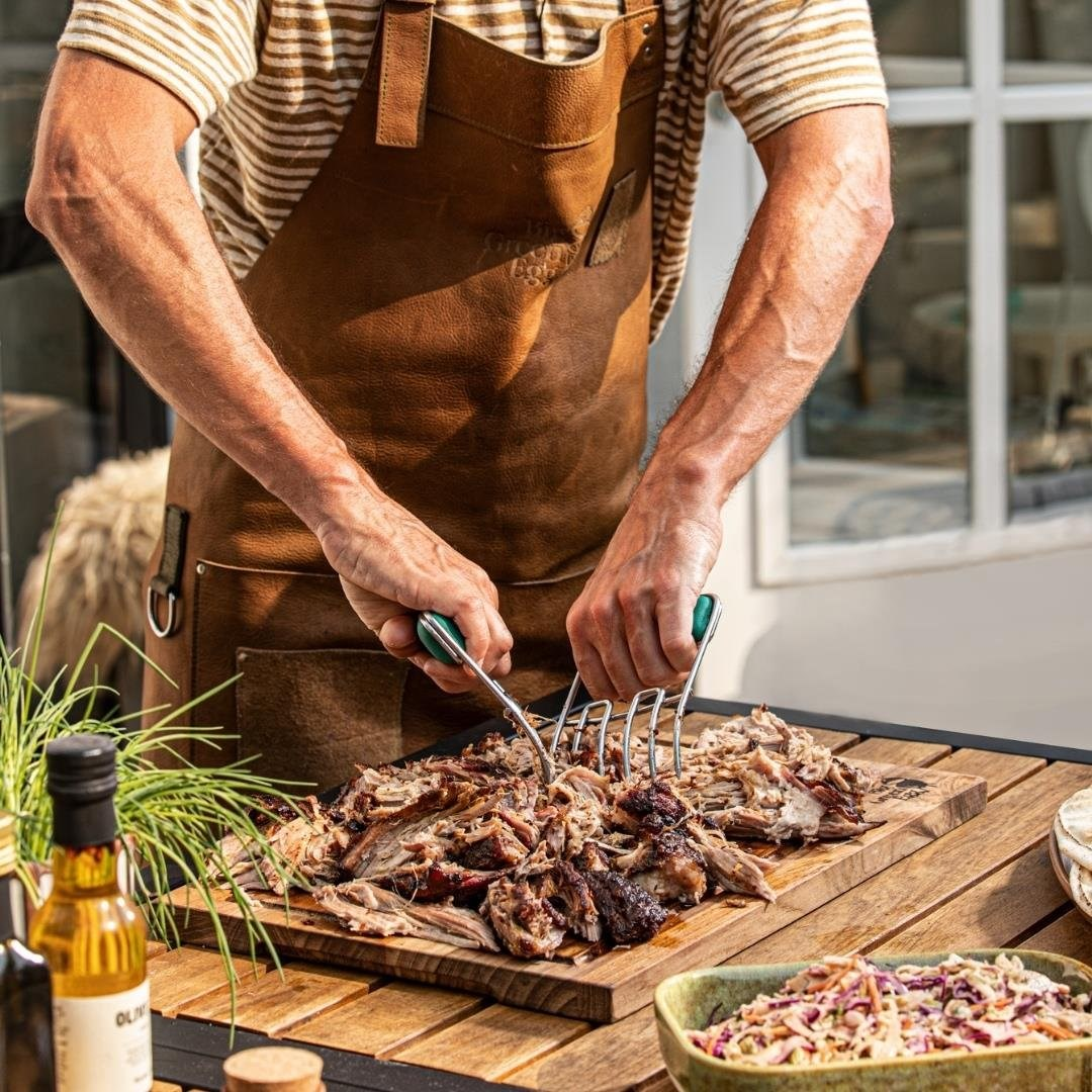 Kahverengi önlüklü adam et pençeleriyle tahta üzerinde pulled pork didikli.