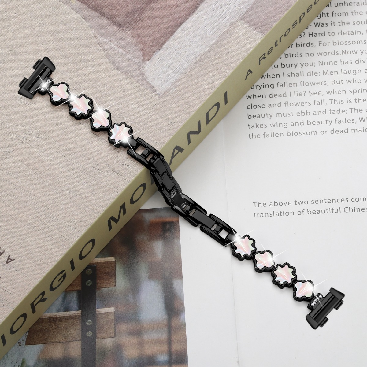 Ein schwarzes Metallarmband mit weißen Blumenanhängern mit rosa Akzenten liegt auf einem Buch.