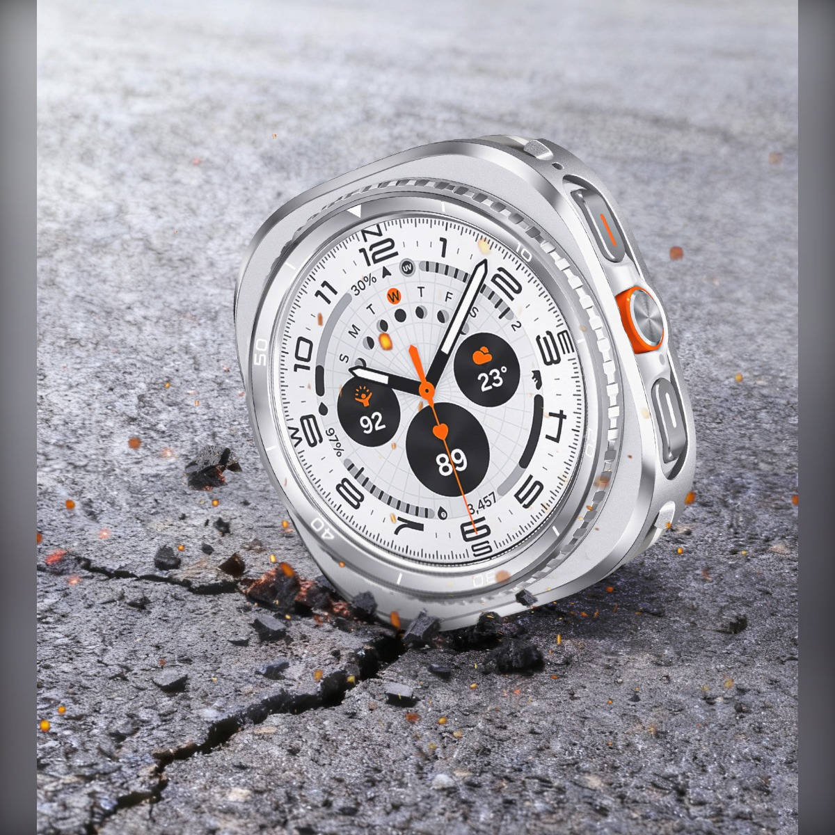 Uno smartwatch argentato con accenti arancioni poggia su asfalto incrinato.