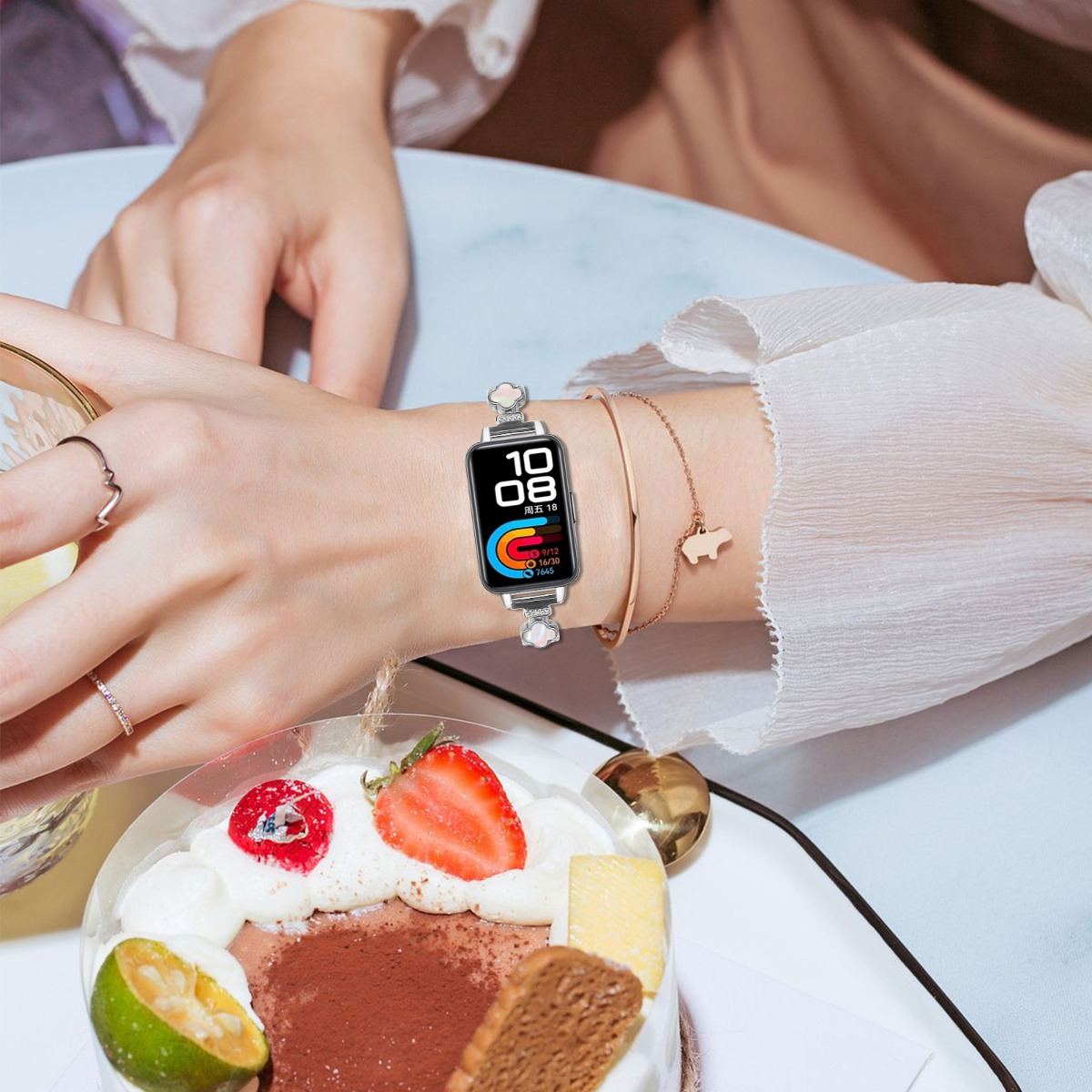 Handgelenk einer Frau mit einer Smartwatch mit buntem Display und silbernem Band, neben einem Dessert.