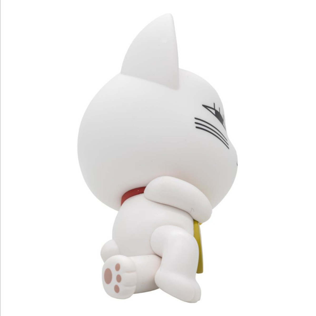 Una figurilla de gato blanco se sienta con las patas recogidas, lleva un collar rojo y un babero amarillo.