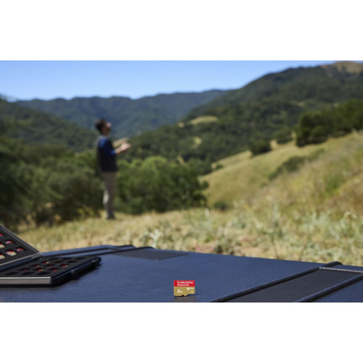 Scheda microSD su superficie scura, persona e colline sullo sfondo.