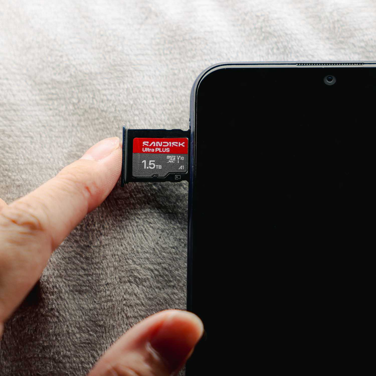 Una mano inserisce una scheda microSD SanDisk Ultra Plus da 1,5 TB nello slot di uno smartphone scuro.