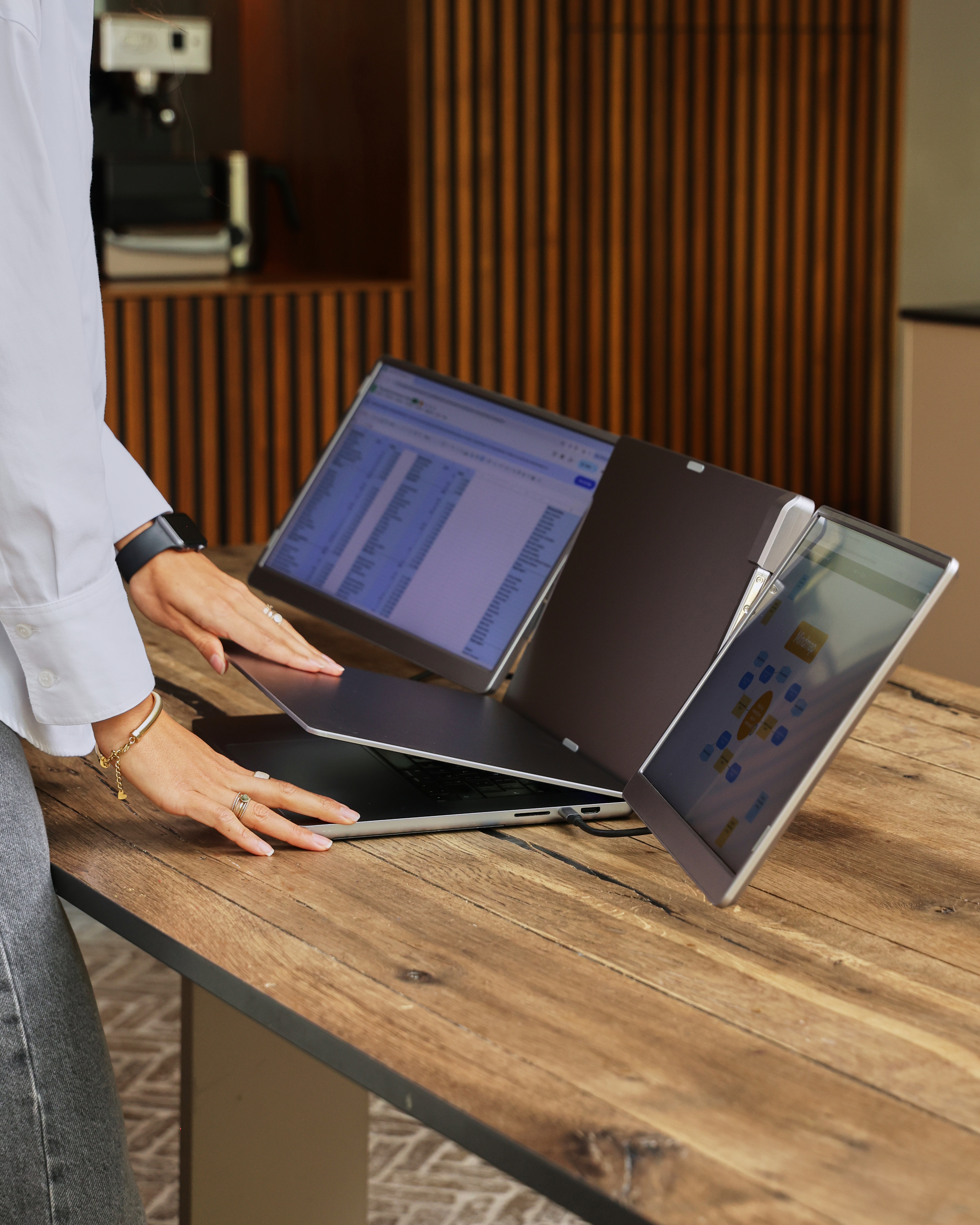 Een persoon in een wit overhemd en grijze broek gebruikt een laptop met twee extra schermen.
