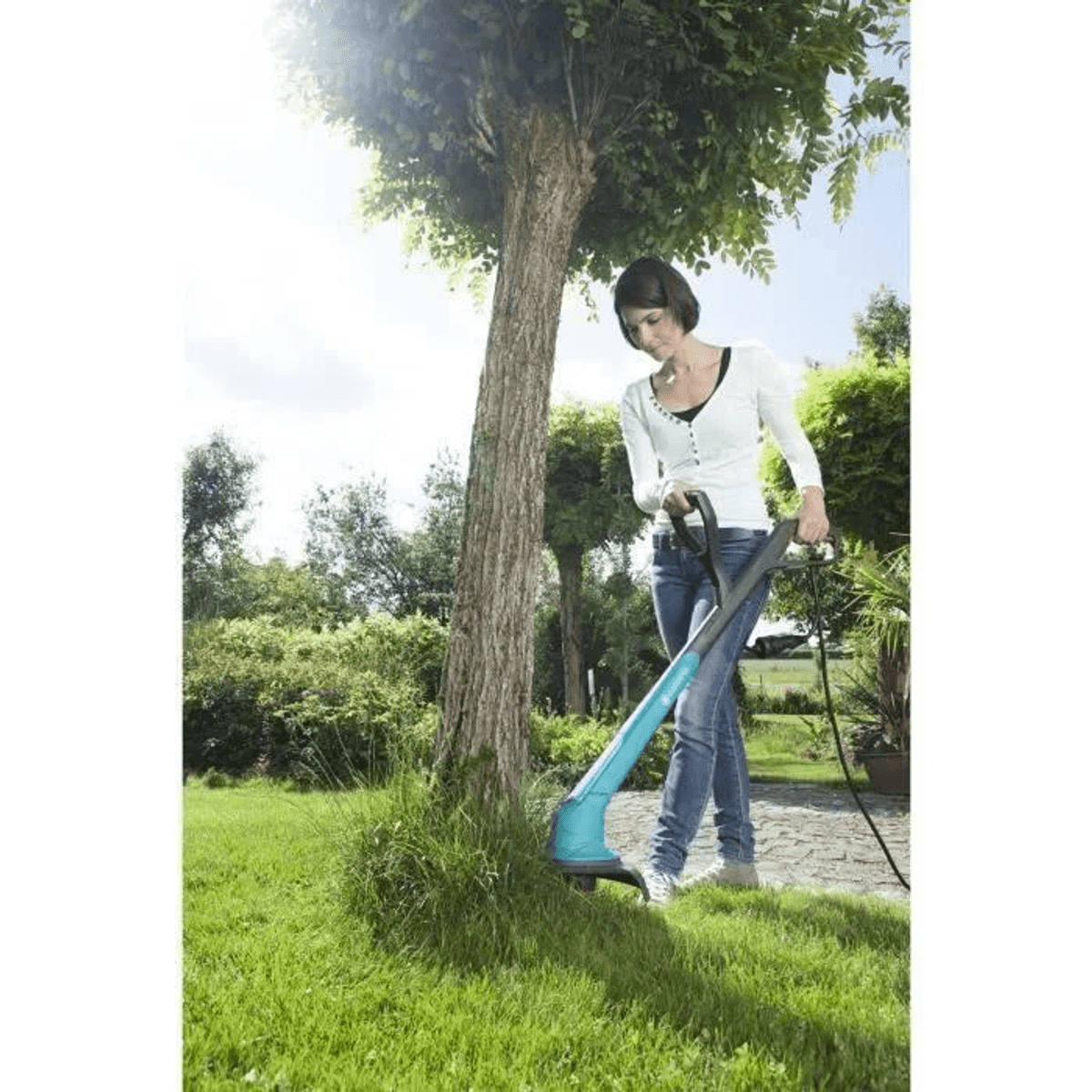 Eine Frau trimmt Gras mit einem Rasentrimmer neben einem Baum.