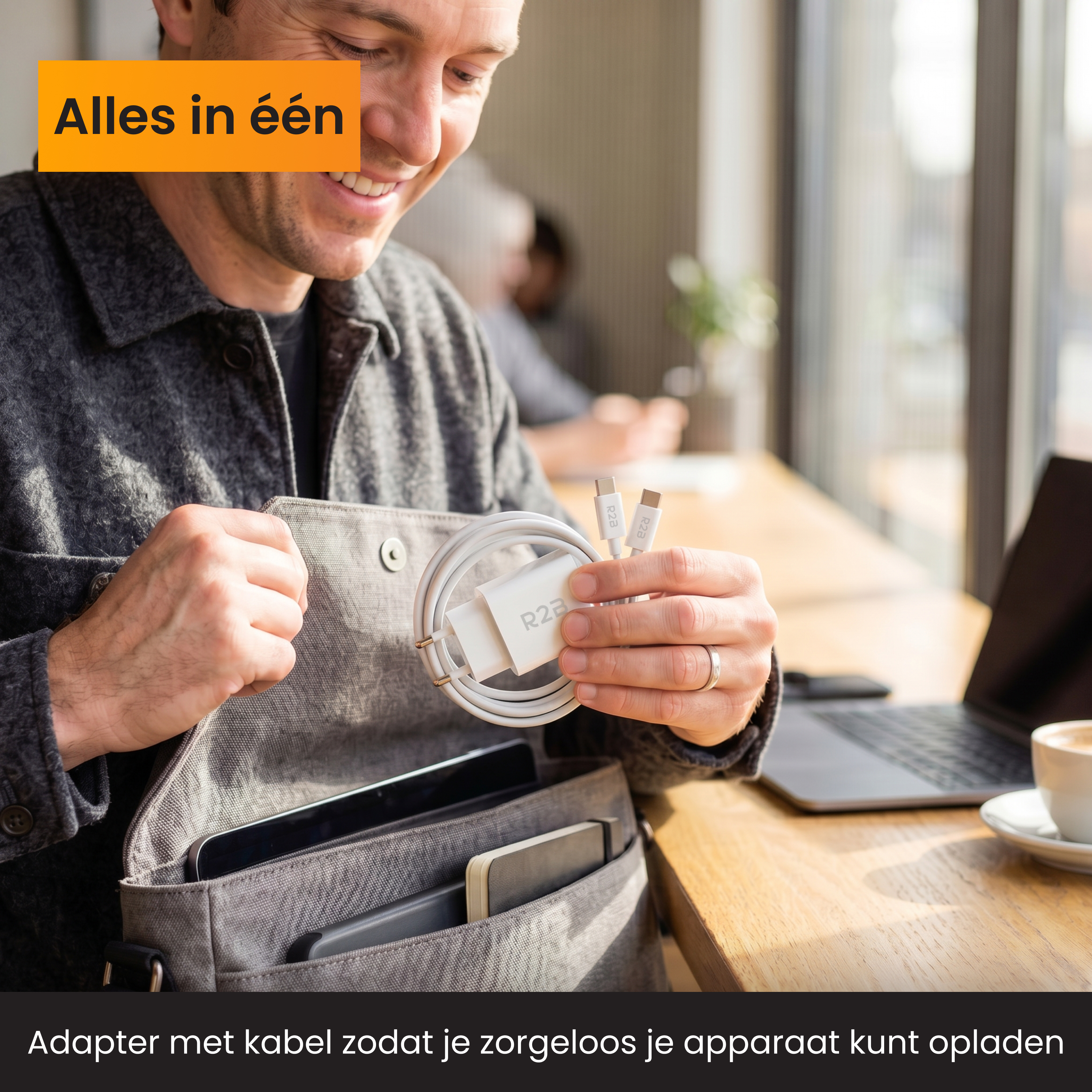 Man houdt witte R2B oplader met kabel vast. Laptop en koffie op achtergrond.