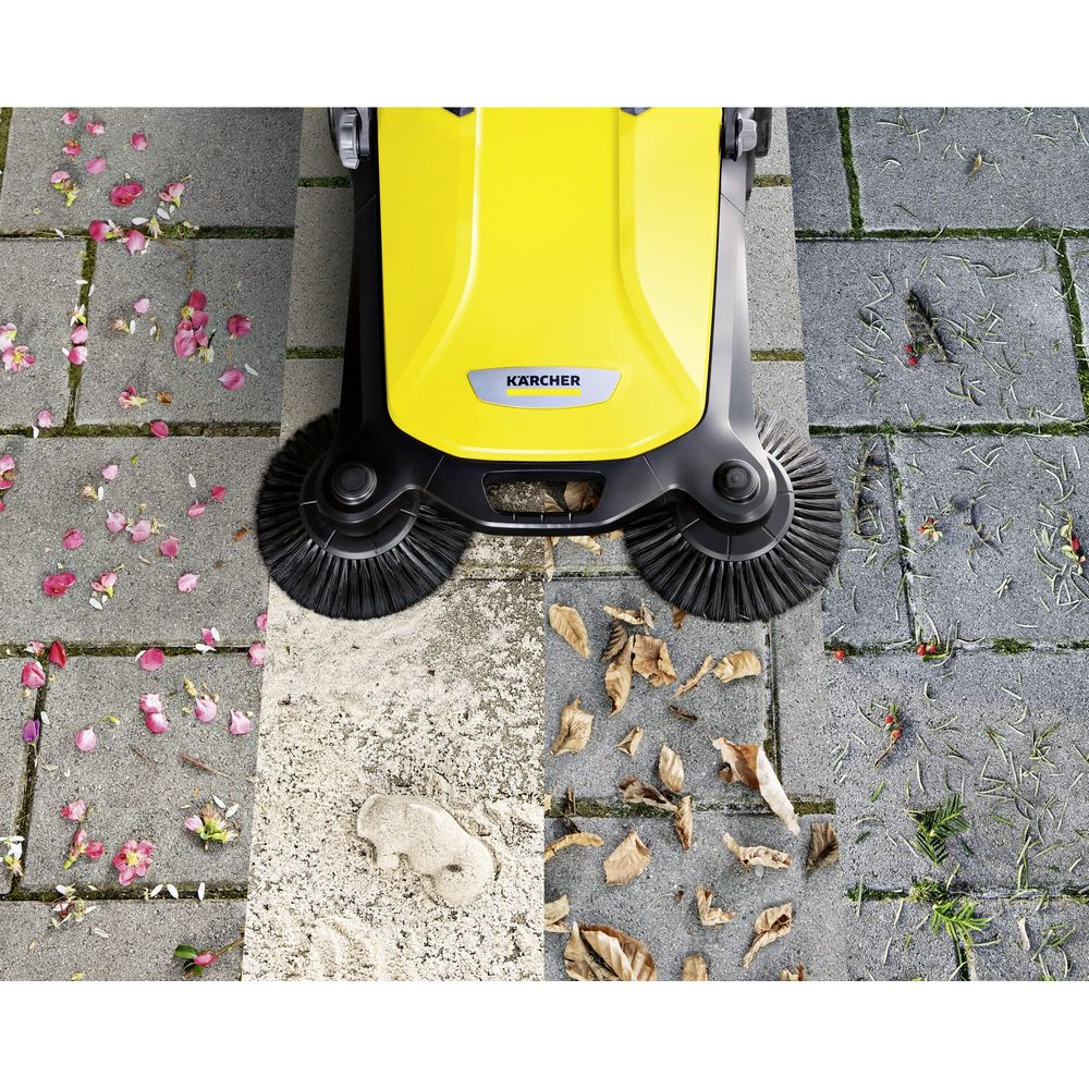 Spazzatrice Karcher gialla su patio in pietra con foglie, petali e detriti sparsi.