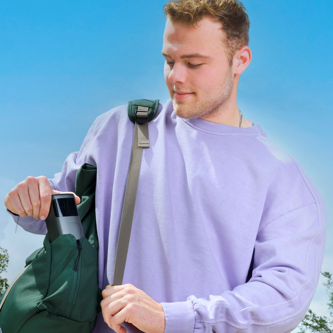 Un uomo in felpa viola mette un dispositivo grigio in una borsa verde.