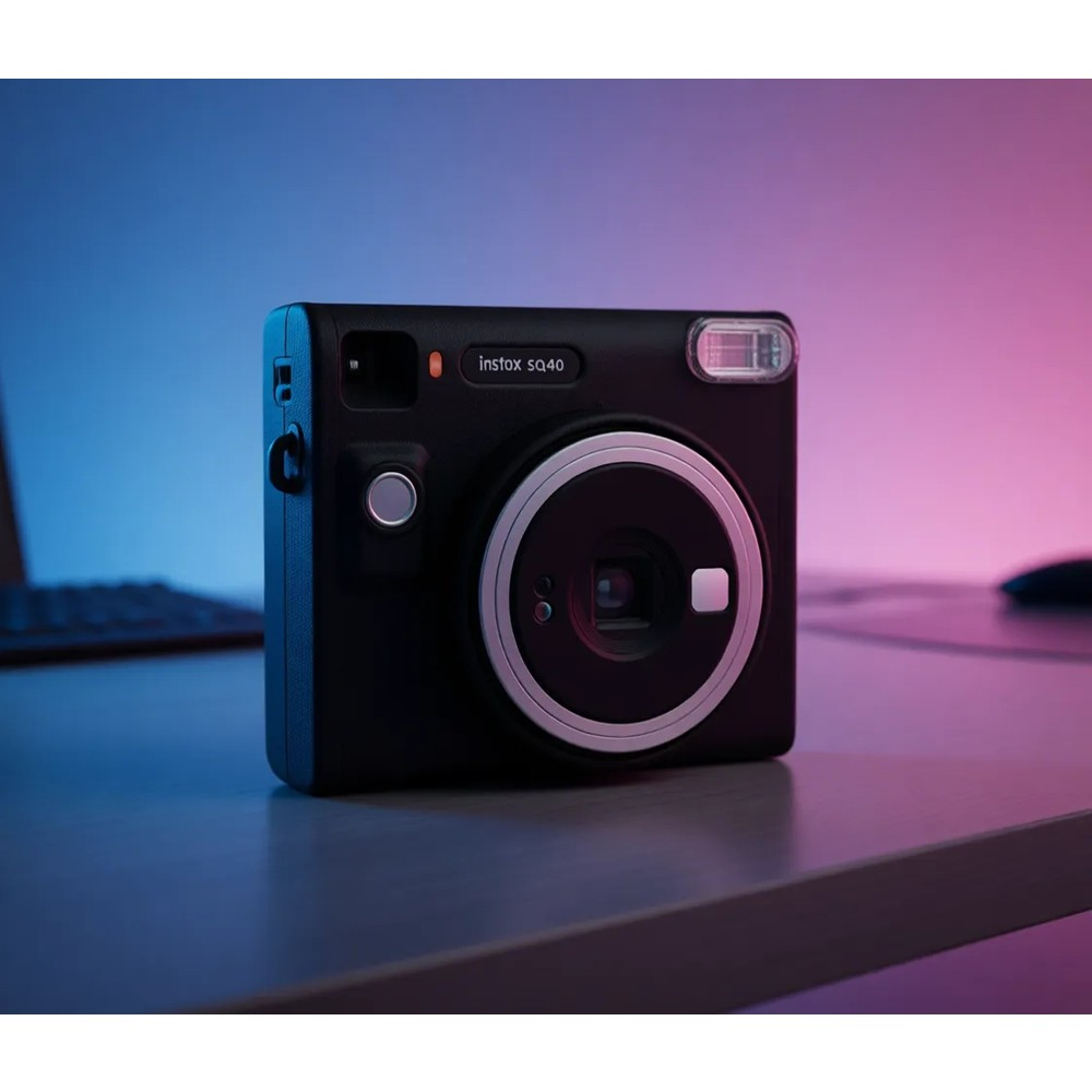 Siyah Instax SQ40 kamera flaşlı ve lensli, masada, arkada mavi-mor ışık var.