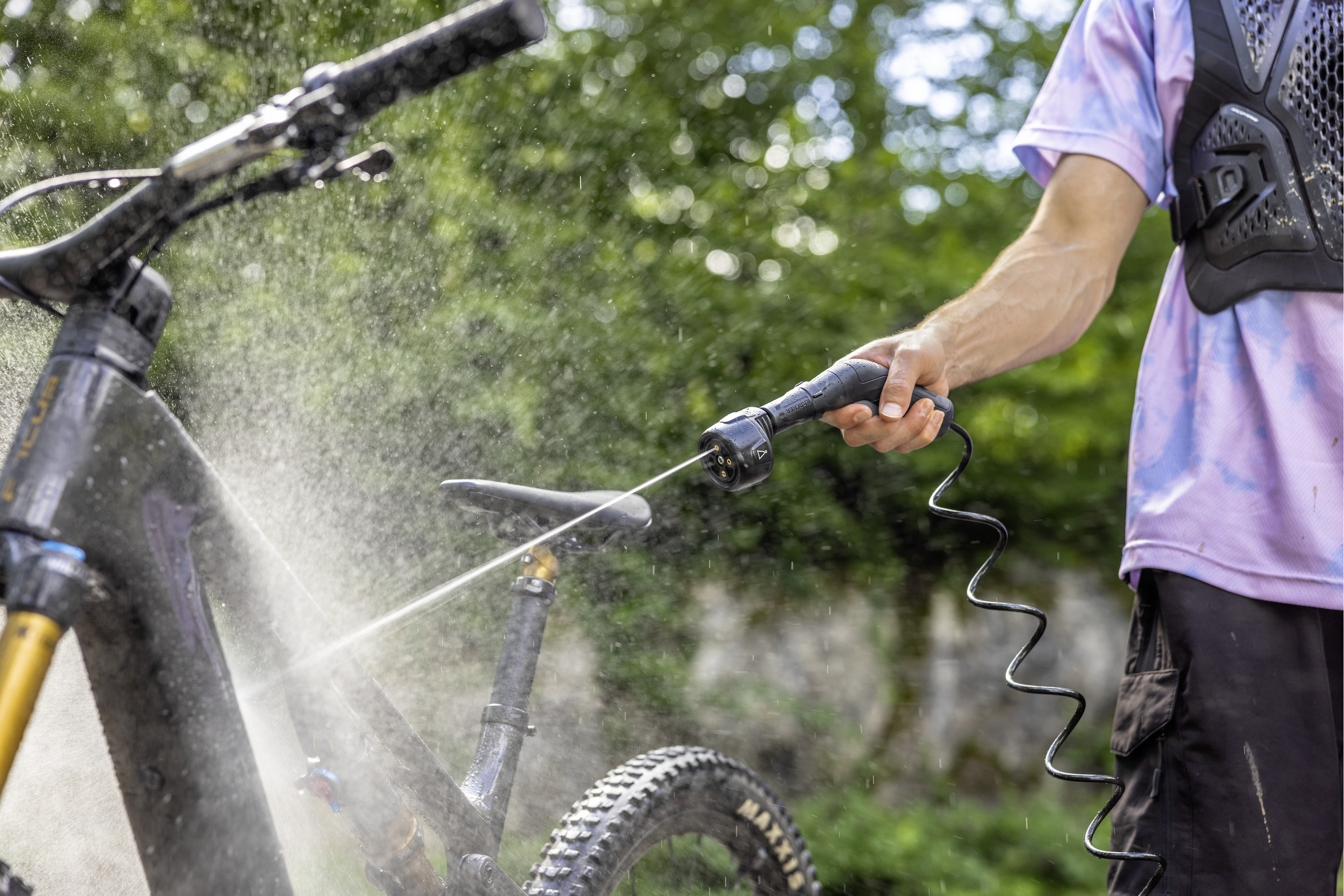 Eine Person wäscht ein dunkles Mountainbike mit einem Schlauch im Freien.