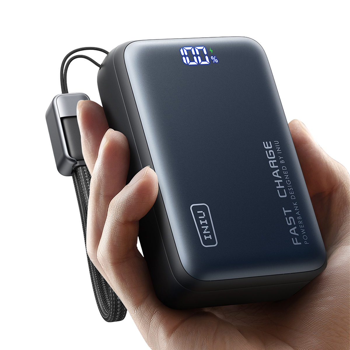 Una mano sostiene un cargador portátil oscuro con 100% de carga y un cordón.
