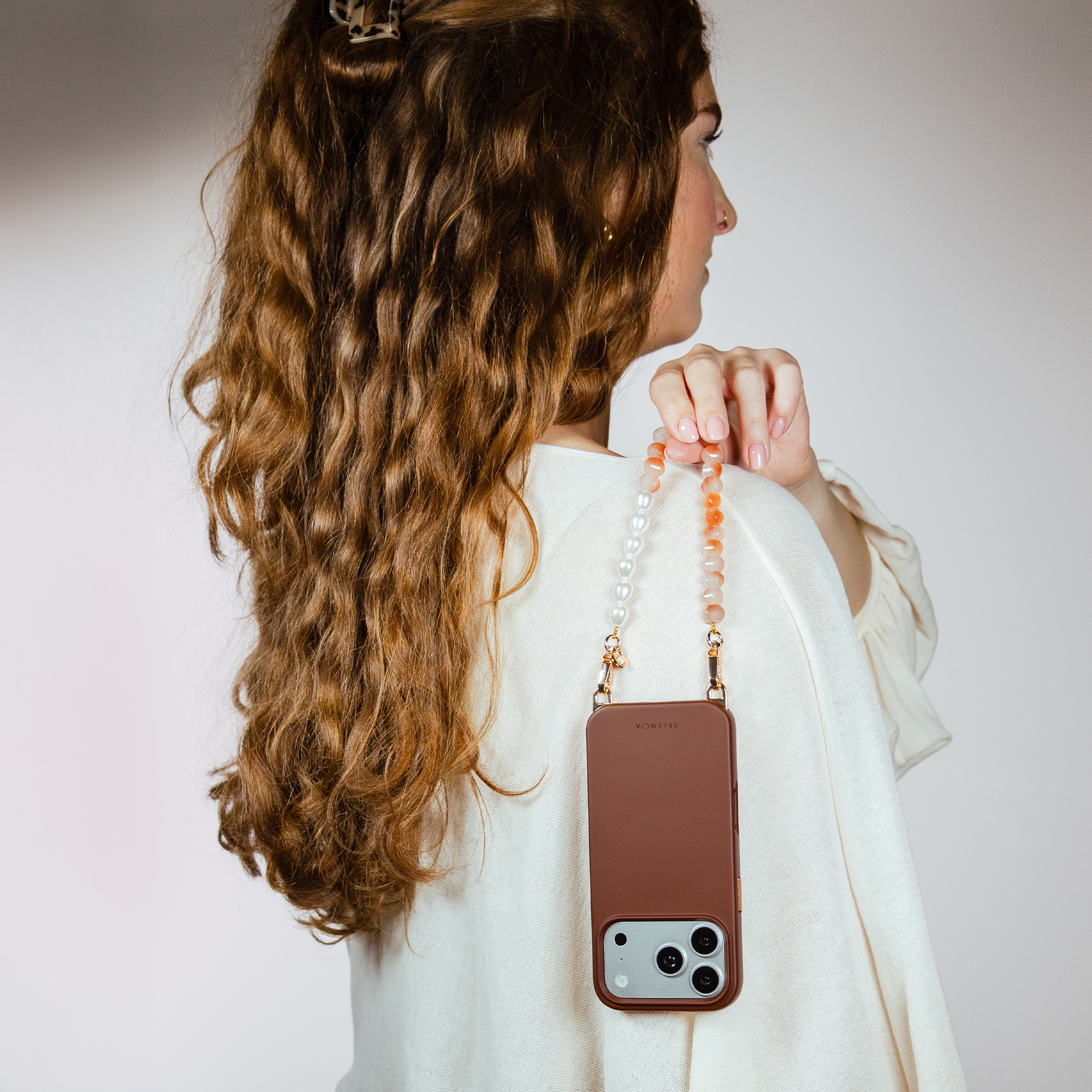Brown phone case with beaded strap on a woman with brown curly hair.