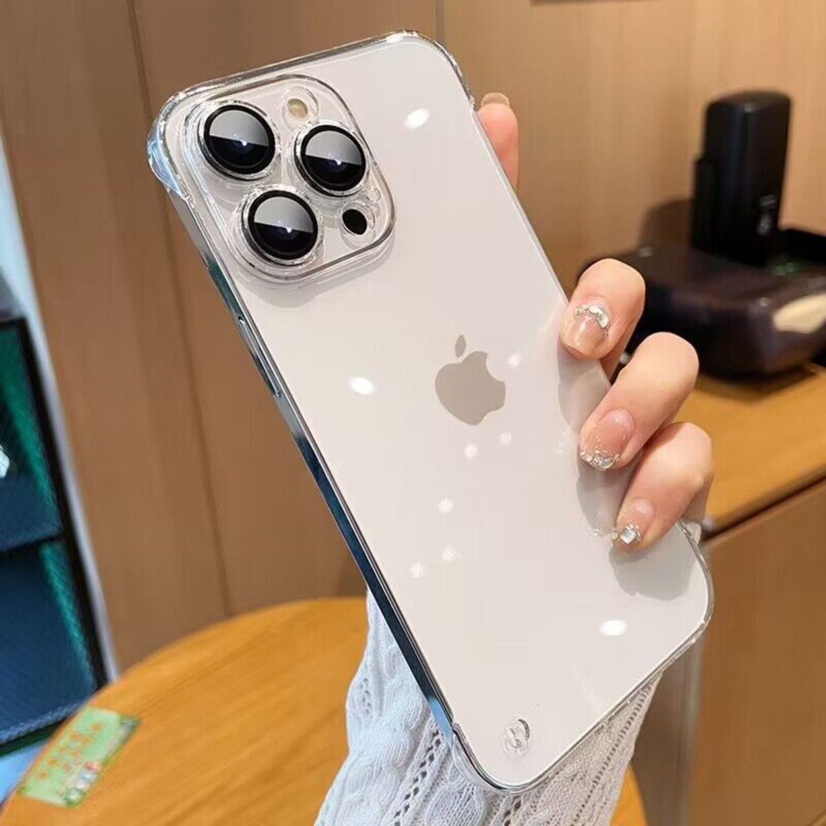 Eine Hand hält ein weißes iPhone mit klarer Hülle, zeigt Kameralinsen und Apple-Logo.