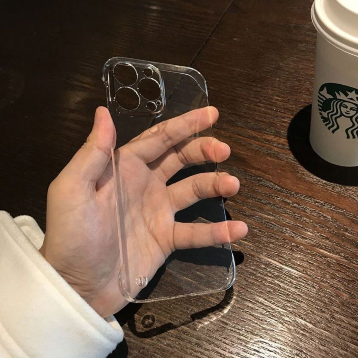 Eine Hand hält eine transparente Handyhülle vor einer braunen Holztischoberfläche.