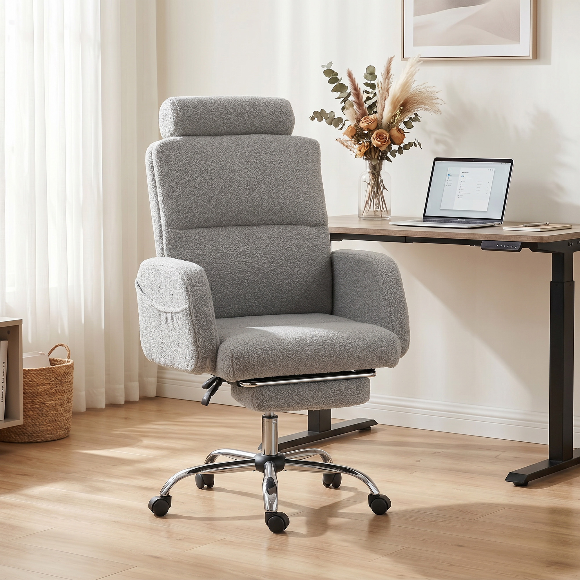 Silla de oficina gris de tela teddy con base cromada y ruedas, junto a un escritorio.