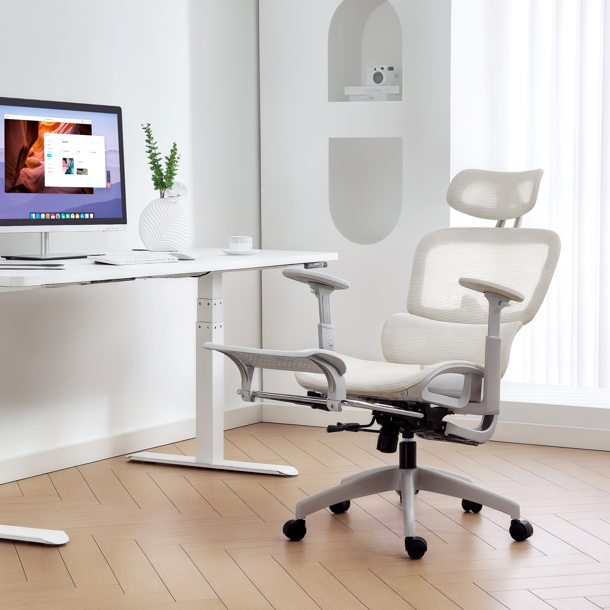 Una silla de oficina de color claro junto a un escritorio ajustable en altura con ordenador.