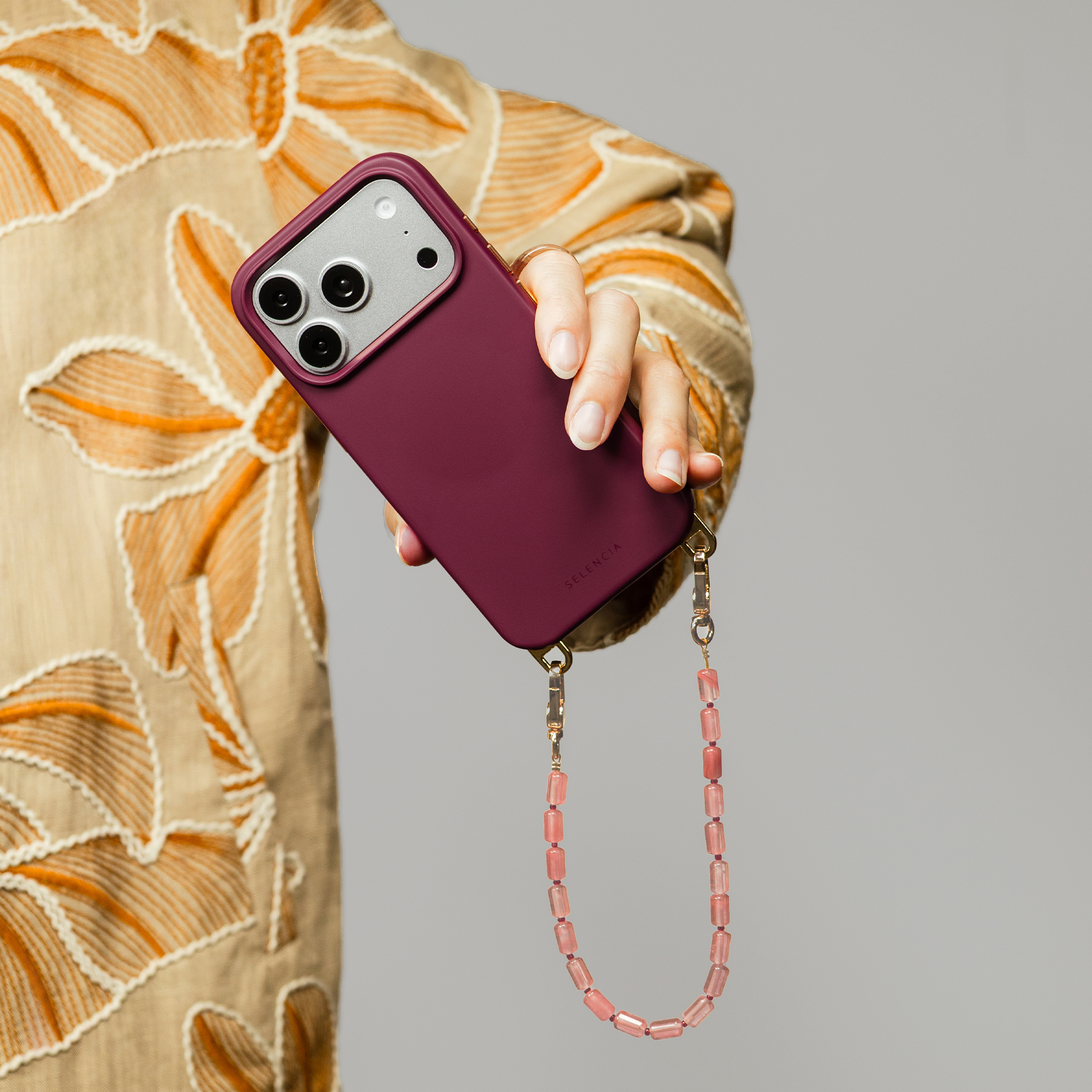 A hand holds a purple phone with a beaded strap attached.