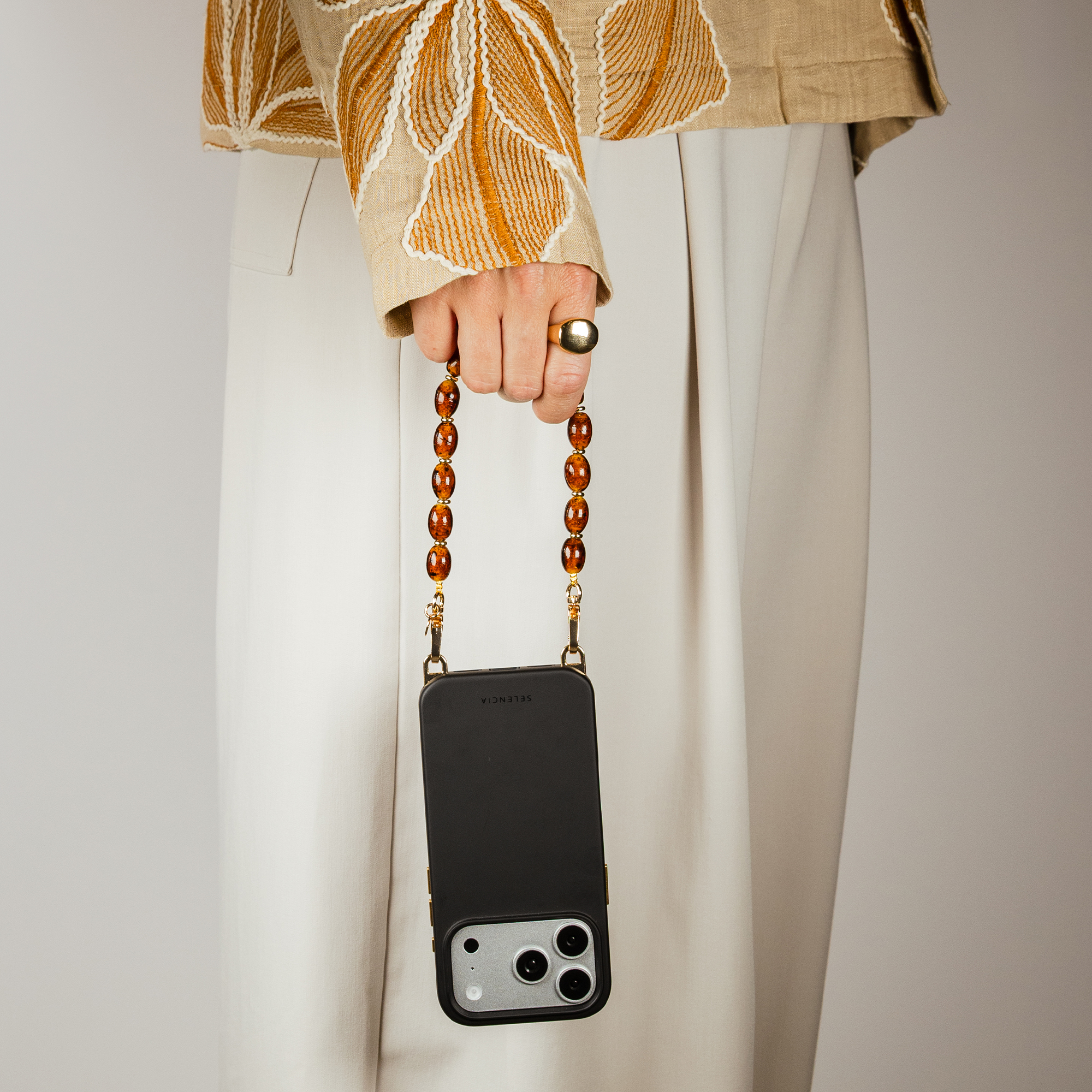A person holds a black phone with a beaded strap. Gold ring.