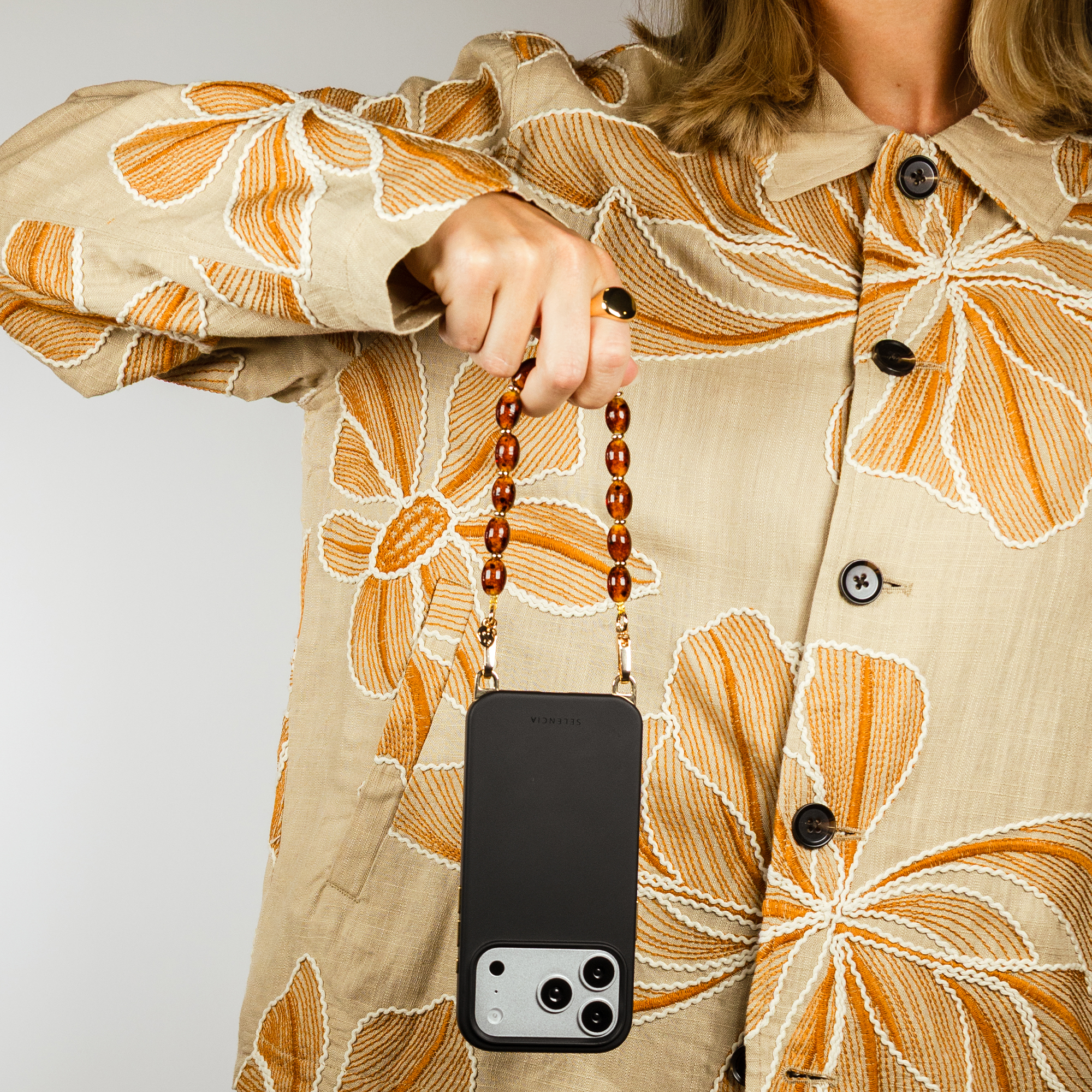Person holding black phone with beaded chain, wearing jacket with floral pattern.