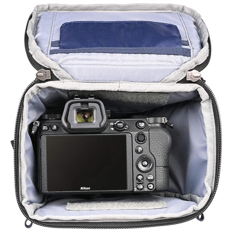 Una cámara Nikon con lente está en un bolso de cámara gris abierto con cremalleras YKK.