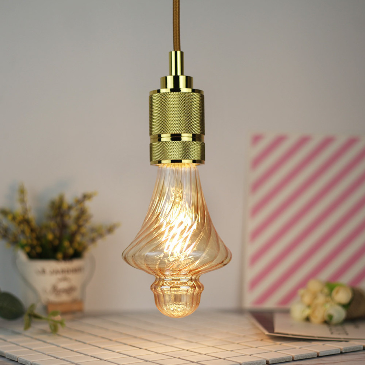 Eine goldene Pendelleuchte mit einer gedrehten Glühbirne und einem warmen Licht.