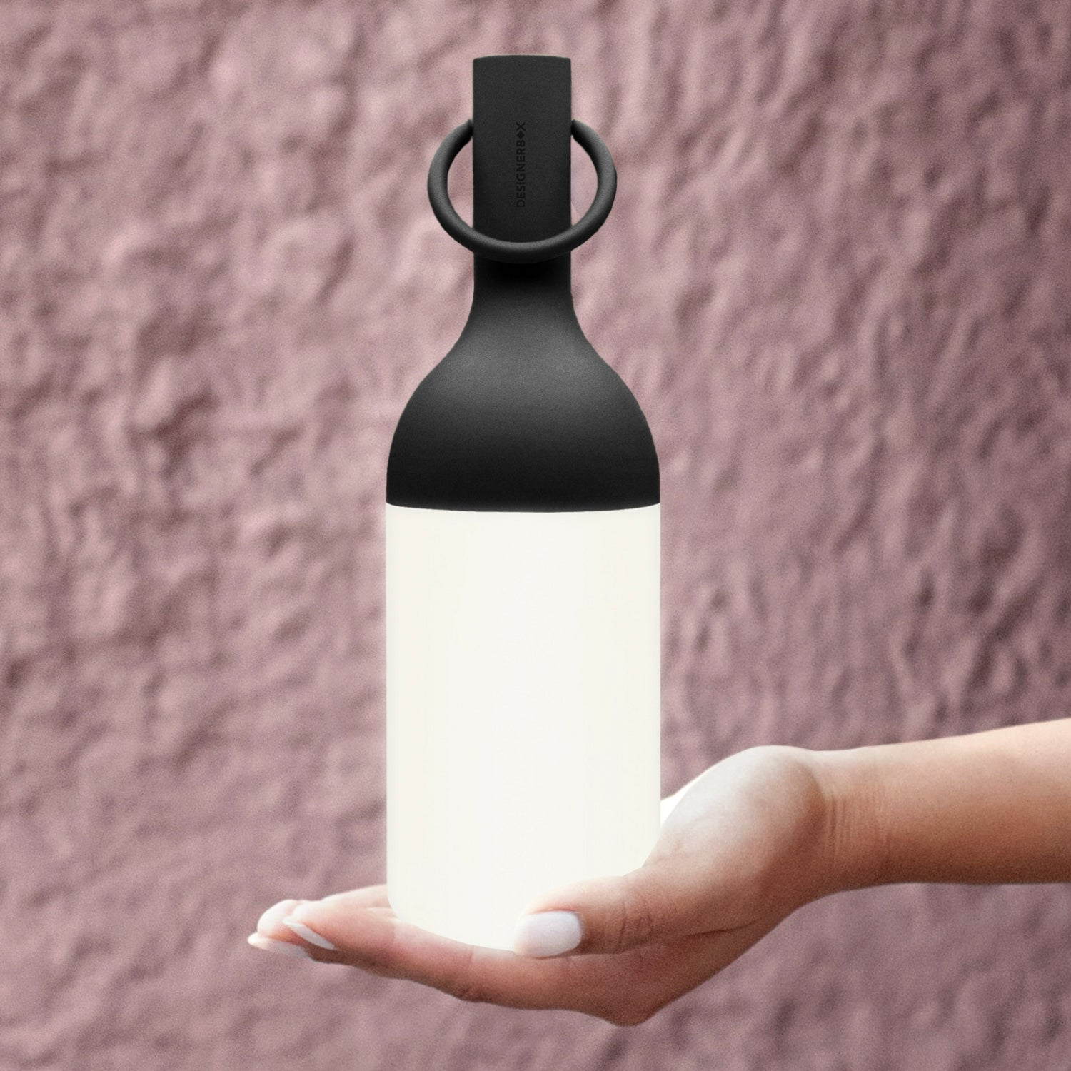Eine Hand hält eine leuchtende, schwarze und weiße Lampe vor einem rosafarbenen Hintergrund.