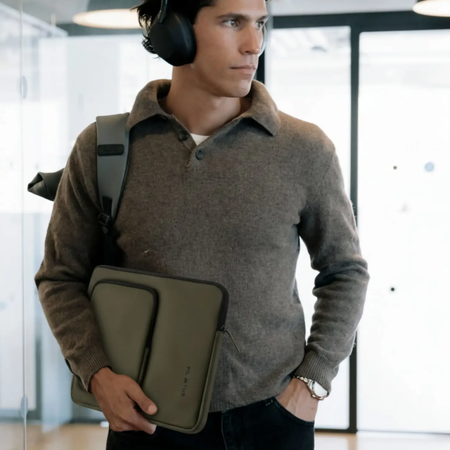Uomo con cuffie e custodia per laptop cammina in ufficio.