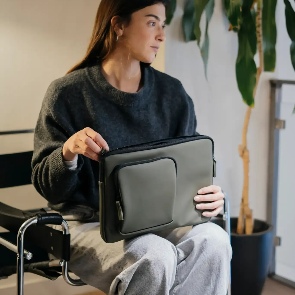 Donna in maglione grigio tiene una custodia verde per laptop con tasca.