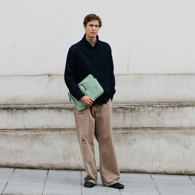 Uomo in camicia scura e pantaloni beige tiene una borsa verde menta.