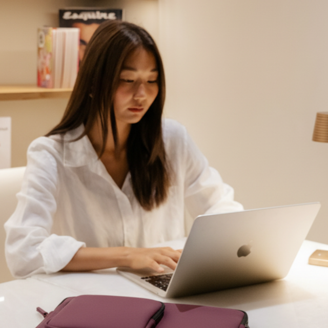 Una donna dai capelli lunghi digita su un laptop. Una custodia viola è in primo piano.