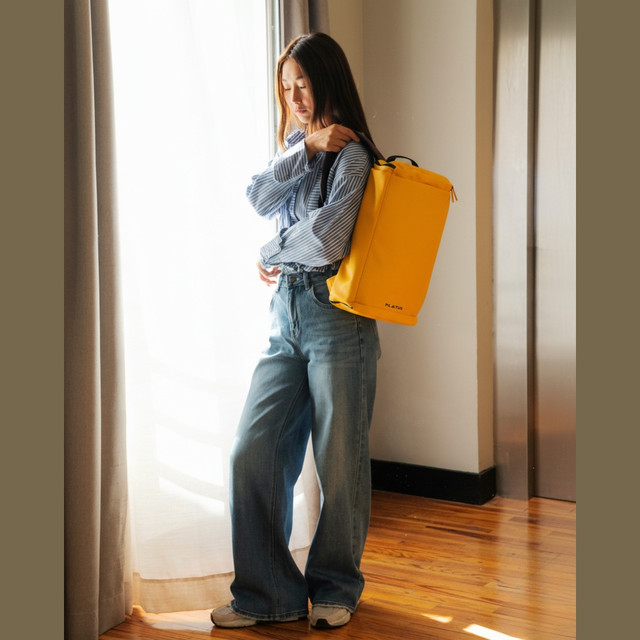 Una donna con zaino giallo in piedi alla luce.
