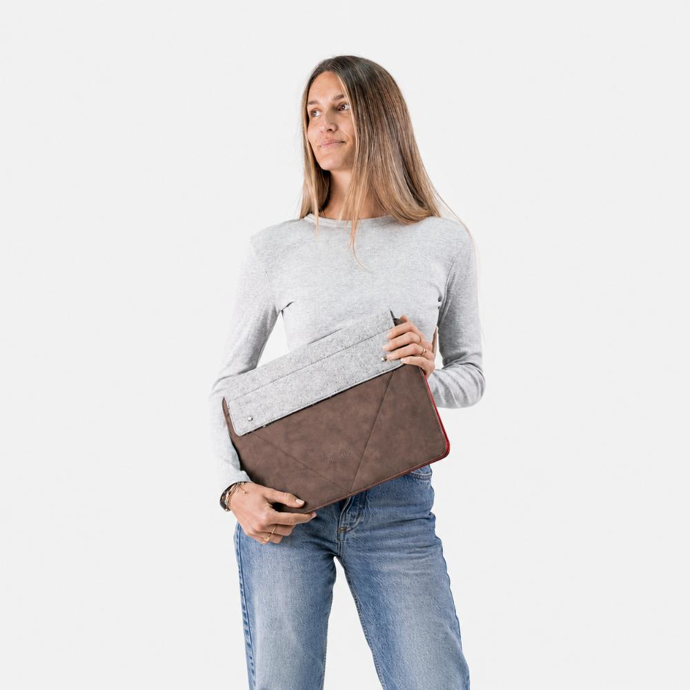 Donna con maglia grigia e jeans tiene una custodia marrone per laptop con fodera rossa.