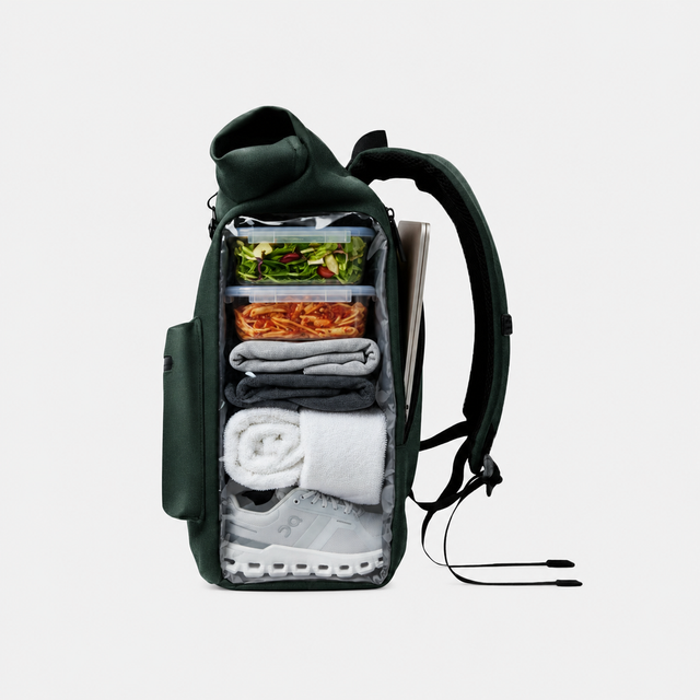 Uno zaino verde scuro è aperto, mostrando cibo, vestiti, una scarpa e un laptop.